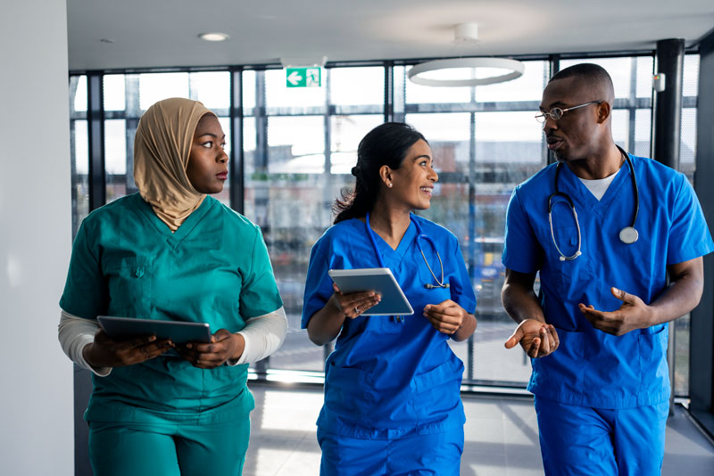 A group of nurses discuss patient care in the hallway of a skilled nursing facility